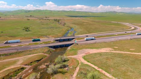 Verdant-central-valley-with-trucks-on-highway,-solar-panels-afar,-sunny-day,-aerial-view