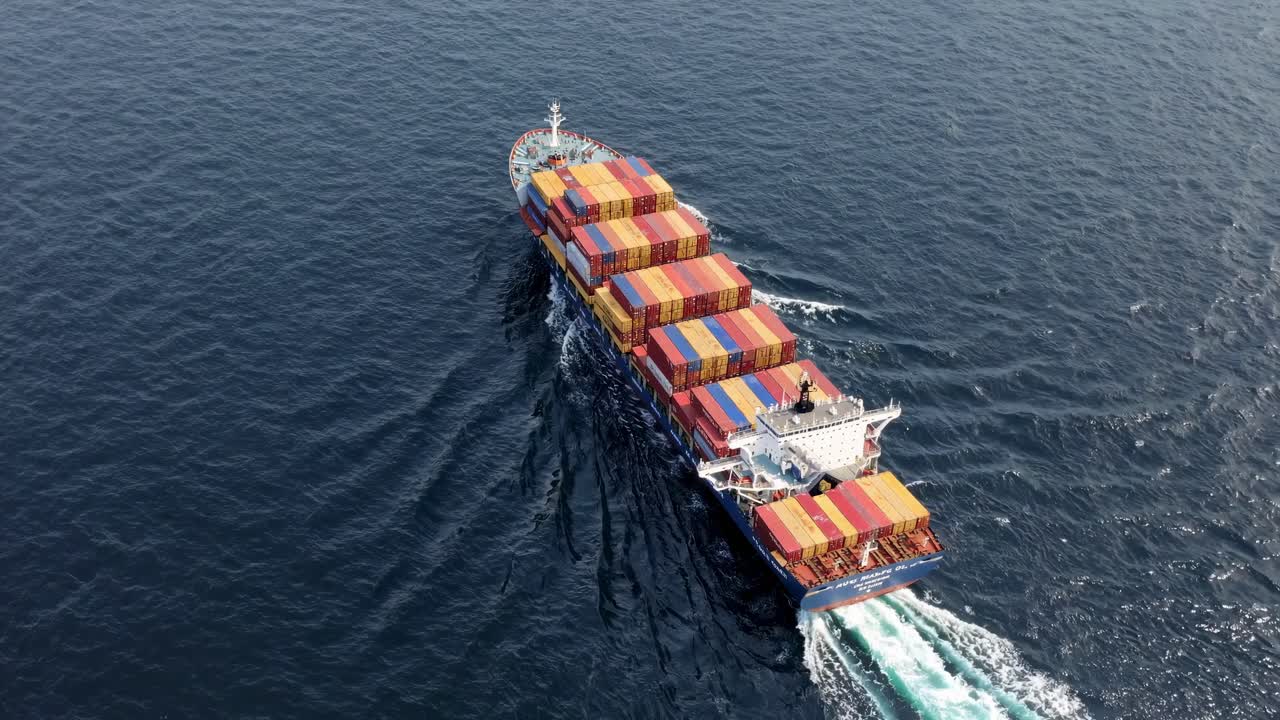 Aerial view of a cargo ship with colorful containers sailing through blue waters, creating a dynamic