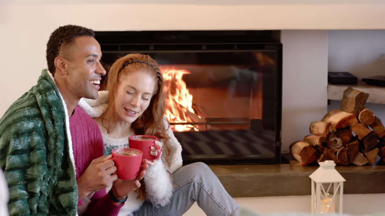 Christmas time, Couple enjoying hot cocoa by cozy fireplace, wrapped in warm blankets, copy space