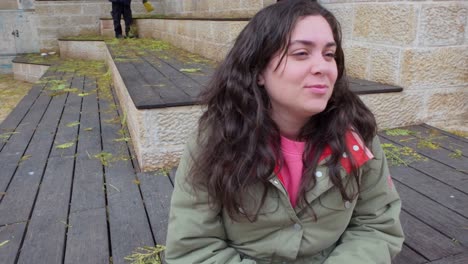 a woman is sitting on a wooden deck, holding a cell phone to her ear