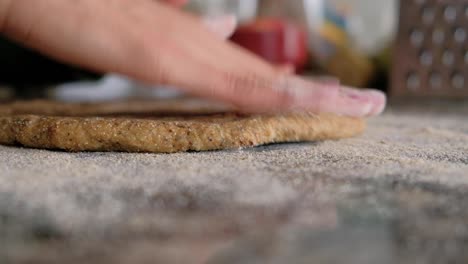 woman sprinkling flour on countertop and stretching the dough with her fingers