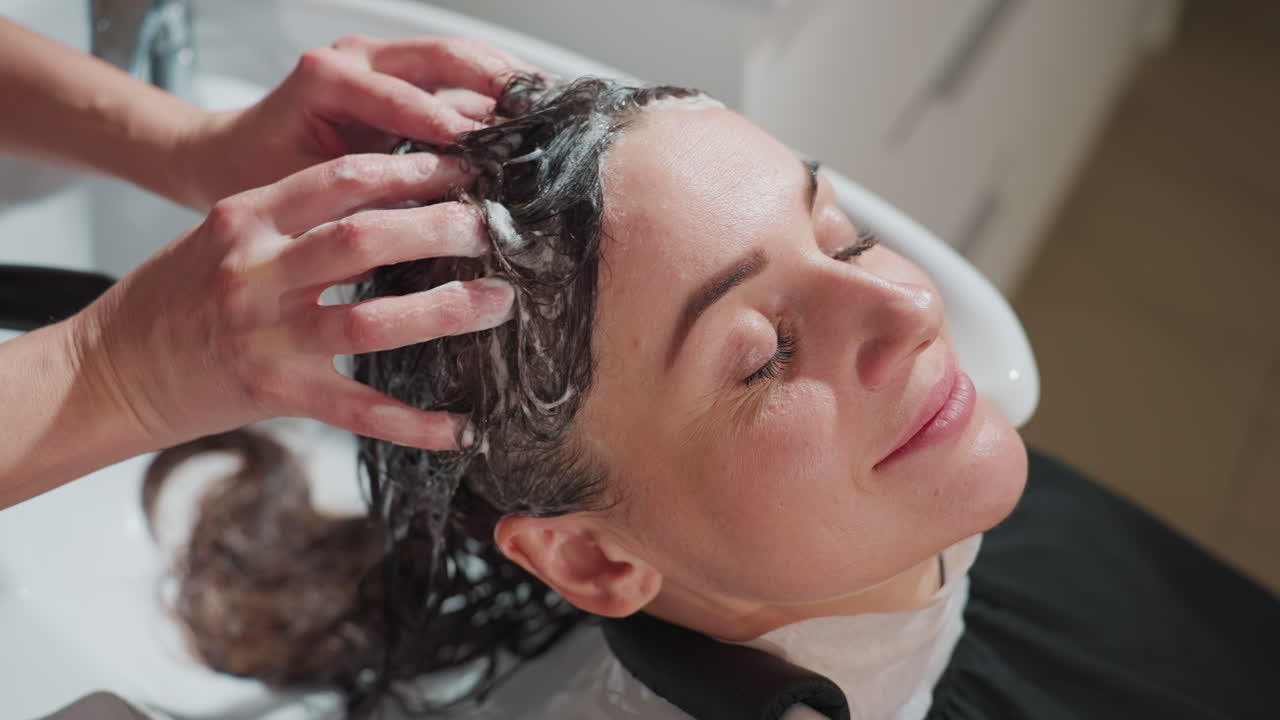 스타일리스트가 부드러운 샴푸 거품을 사용하고, 은은한 조명과 평온한 분위기로 편안한 살롱 환경을 조성하며, 부드러운 마사지와 샴푸를 통해 평화로운 헤어 스파 경험을 제공해요.