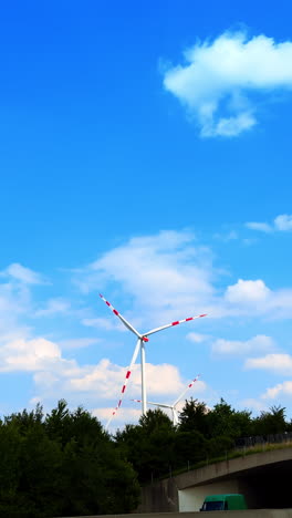 wind turbine in clear blue sky. a wind turbine spins against a bright sky, surrounded by green trees on a sunny day