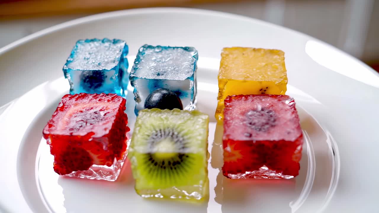 Refreshing and colorful ice cubes made with various fruits like kiwi, strawberry, and blueberries are melting on a white plate, creating a visually appealing and delicious treat