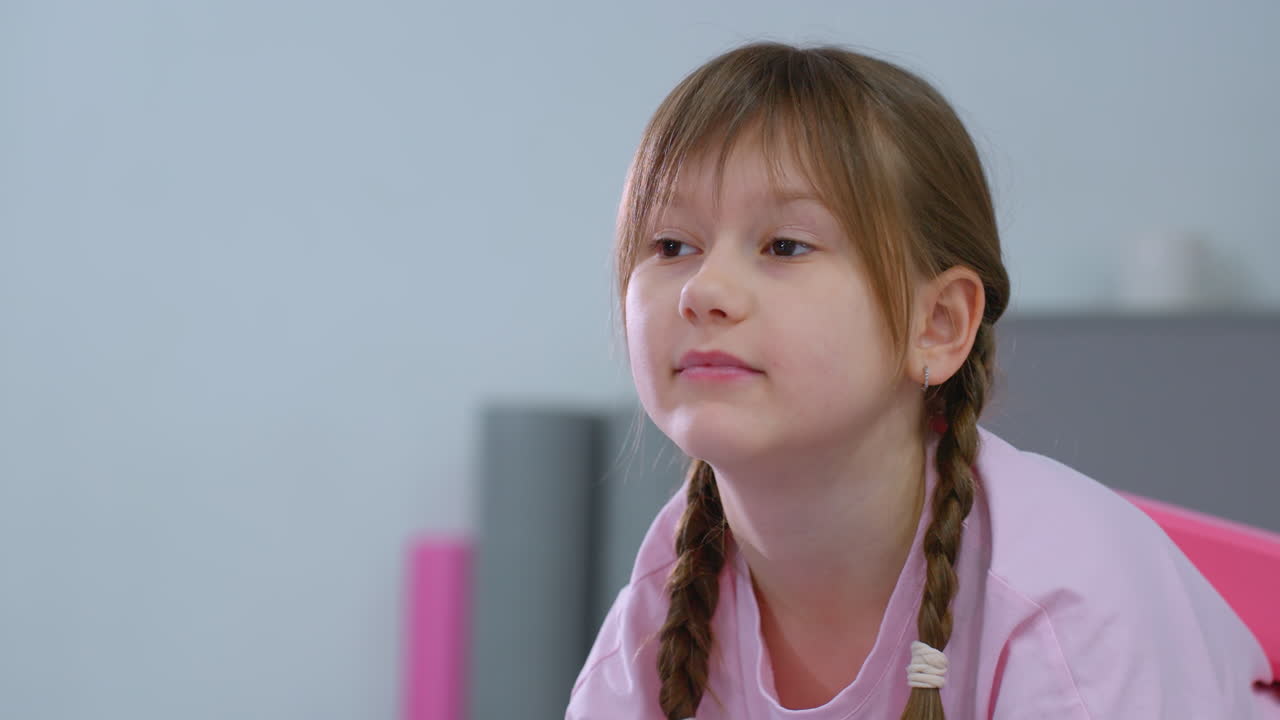 niño pequeño con el cabello atado estirando la mano hacia adelante mientras equilibra el bloque rosa en la espalda, centrándose en la alineación del cuerpo y la postura en la sesión de entrenamiento