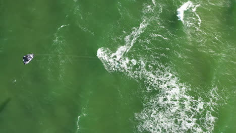 aerial: top view of surfer riding waves on a green colour baltic sea