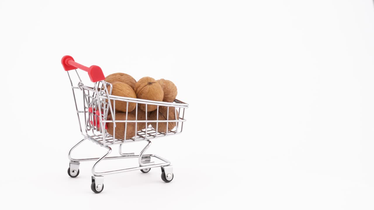 Nákupní vozík plný vlašských ořechů pohybující se vpřed. Izolováno na bílém pozadí. Detail. Makro.