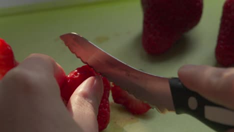 Female-Hand-Cutting-Top-Off-Strawberry-then-Slicing-Down-the-MIddle-in-Slow-Motion