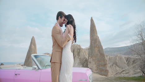 romantic couple posing in front of a pink car at cappadocia