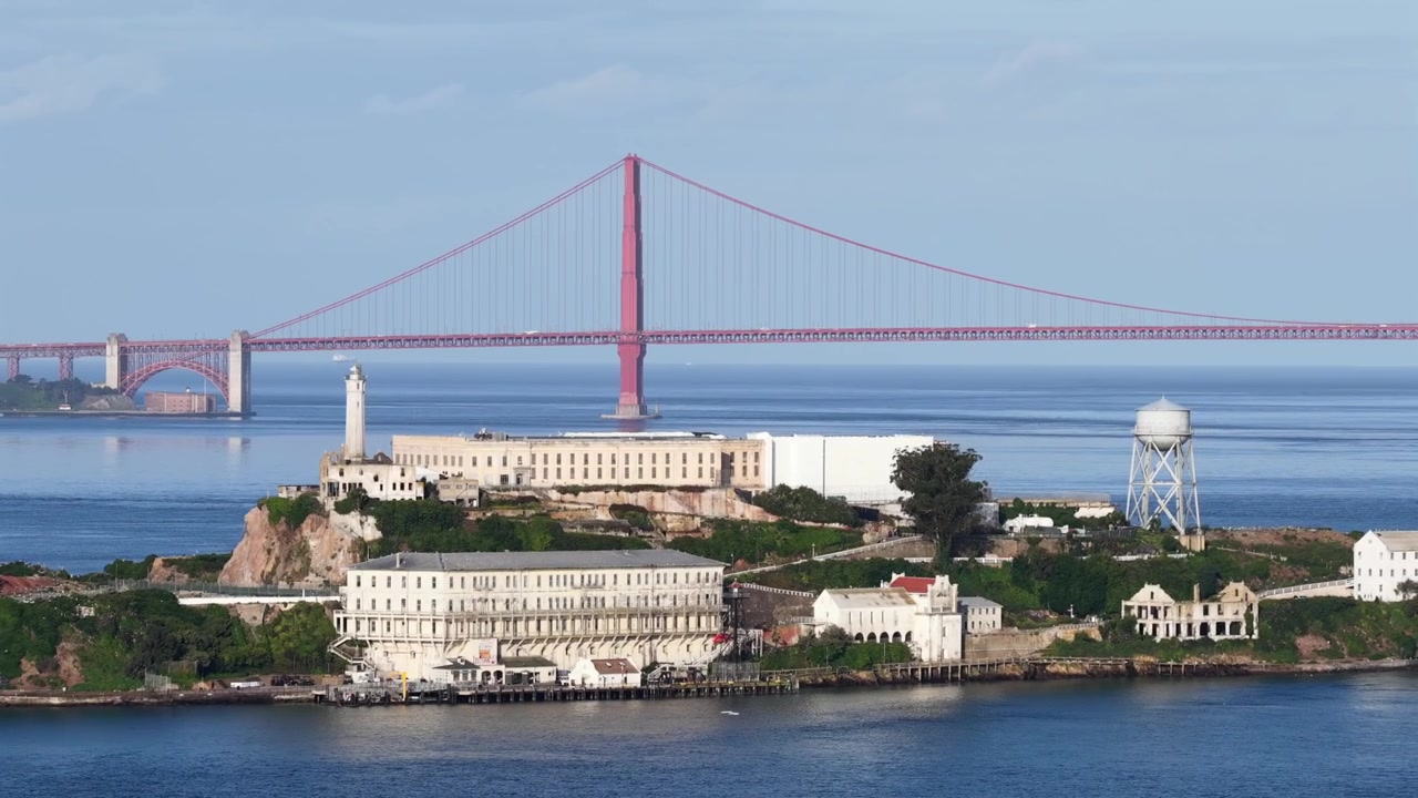 Kaliforniya, San Francisco Körfezi'nde güneşli bir günde ikonik Golden Gate Köprüsü'ne karşı ön planda tarihi deniz feneri ve su kulesi ile Alcatraz Adası. Havadan geniş çekim. Huzurlu banliyö bölgesi.