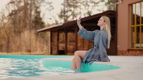 beautiful female visitor of thermal spa complex is taking selfie by mobile phone in outdoor pool