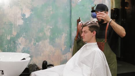 retrato de un hombre adulto que está recibiendo su corte de pelo por un barbero barbudo que está recortando el cabello
