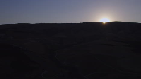 Silhouette-of-wind-turbines-on-a-mountain-at-sunset---rising-up-and-revealing-the-sun