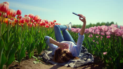 young woman using mobile phone at walk in beautiful blooming park in sunny day.