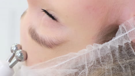 Closeup Vertical Shot of Beautician Performing Mesotherapy Treatment with Specialized Equipment. Close-up vertical shot of beautician performing mesotherapy treatment with specialized equipment, targeting wrinkle reduction and skin rejuvenation on female client forehead. Shooting in