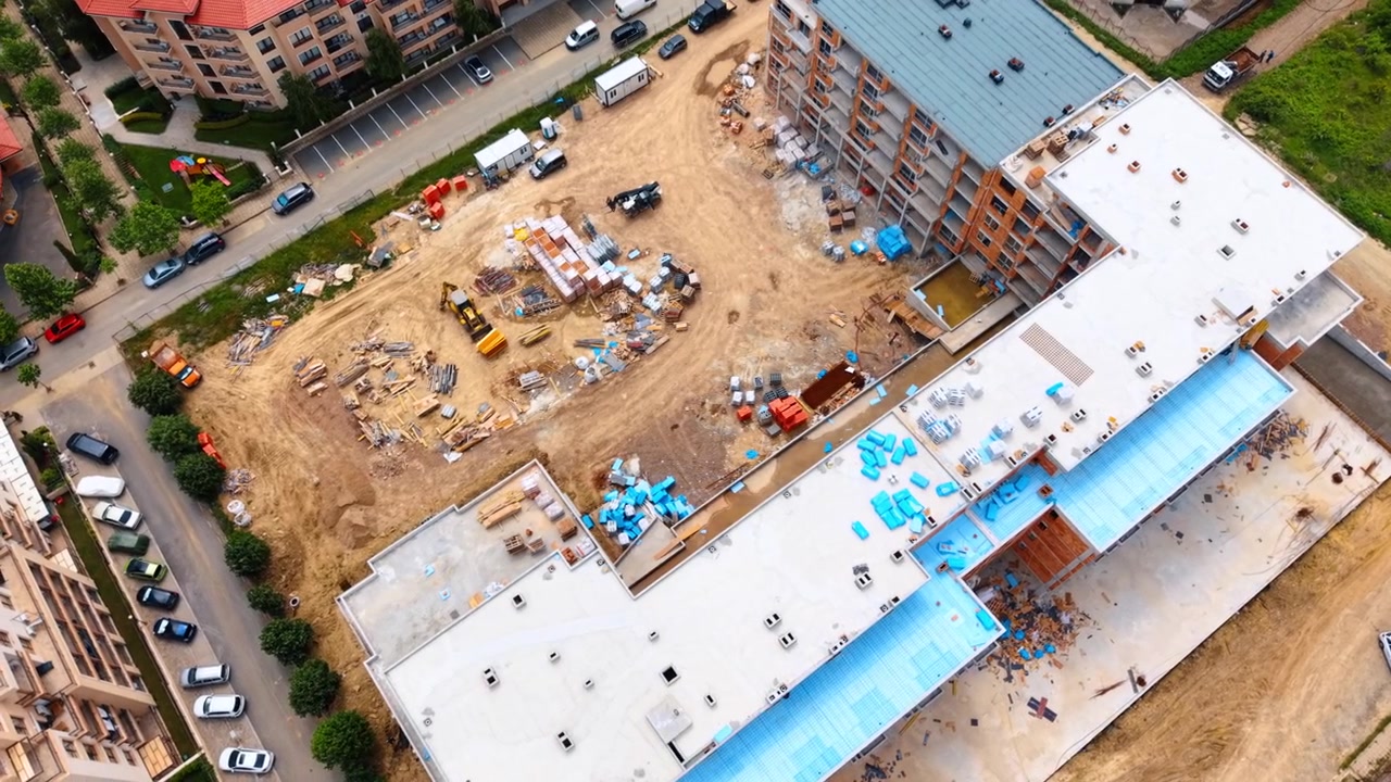 Vista aerea di un cantiere con edificio e isolamento blu. Vista dall'alto di un cantiere edile attivo con struttura in cemento, pannelli isolanti blu e macchinari.