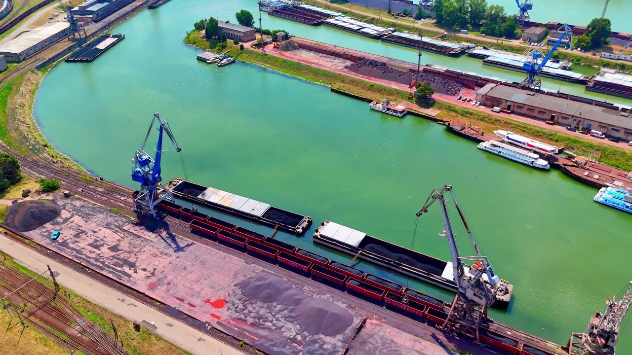 Porto fluviale industriale con chiatte da carico, Bratislava, Slovacchia. Vista dall'alto di banchine di carico e gru al lavoro sulle acque verdi del Danubio