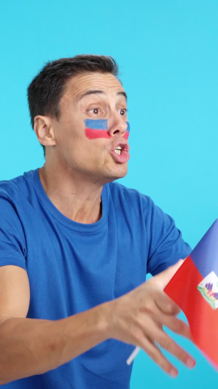 Man cheering for Haiti waving a national flag looking away