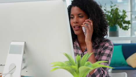 Female-executive-talking-on-mobile-phone-while-working-on-computer-at-desk-4k