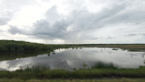 POV-from-moving-vehicle-along-wetlands-with-rain-in-the-background-and-large-pool-of-water-in-foreground