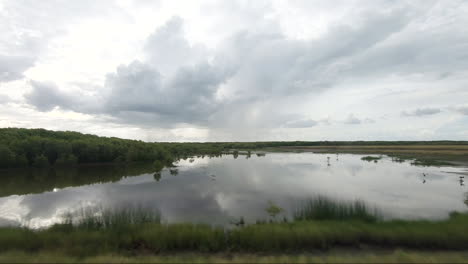 POV-Von-Einem-Fahrenden-Fahrzeug-Entlang-Von-Feuchtgebieten-Mit-Regen-Im-Hintergrund-Und-Einem-Großen-Wasserbecken-Im-Vordergrund