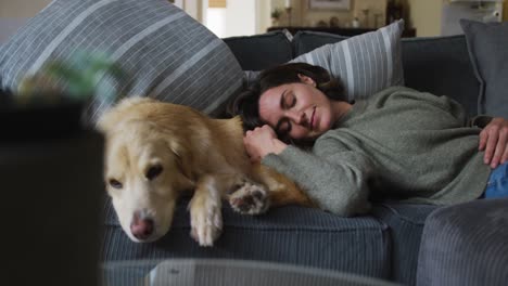 Smiling-caucasian-woman-stroking-her-pet-dog-on-sofa-next-to-her