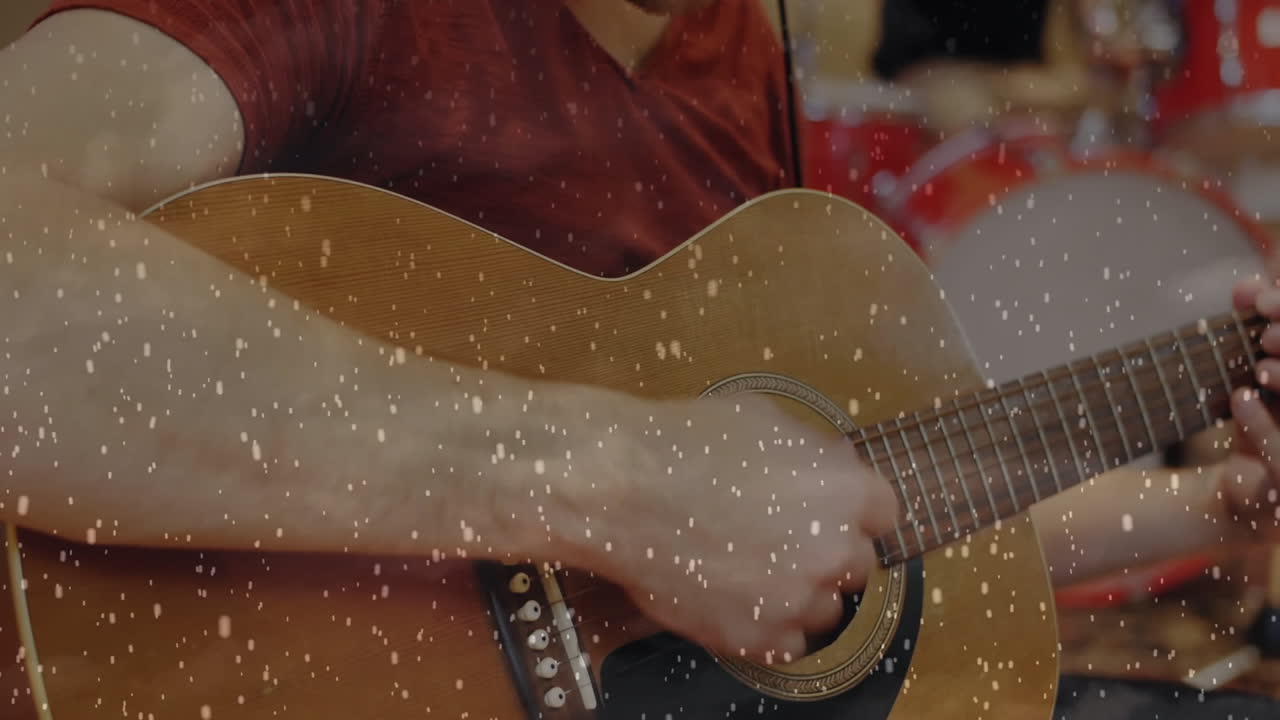 Male guitarist strumming acoustic guitar near drummer in music studio displaying film grain overlay