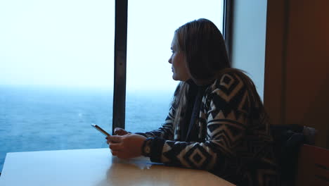 woman looking at phone and out of window on a ferry