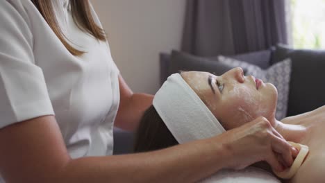 caucasian woman lying back while beautician gives her a facial