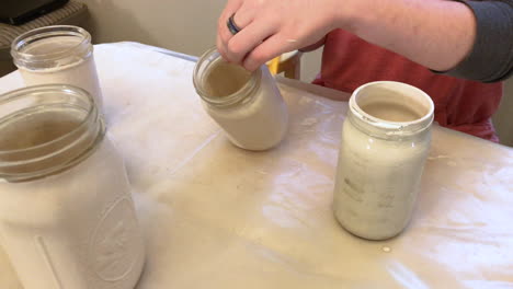 camera zooming in on a person recycling and upcycling mason jars by painting them and turning them into vases