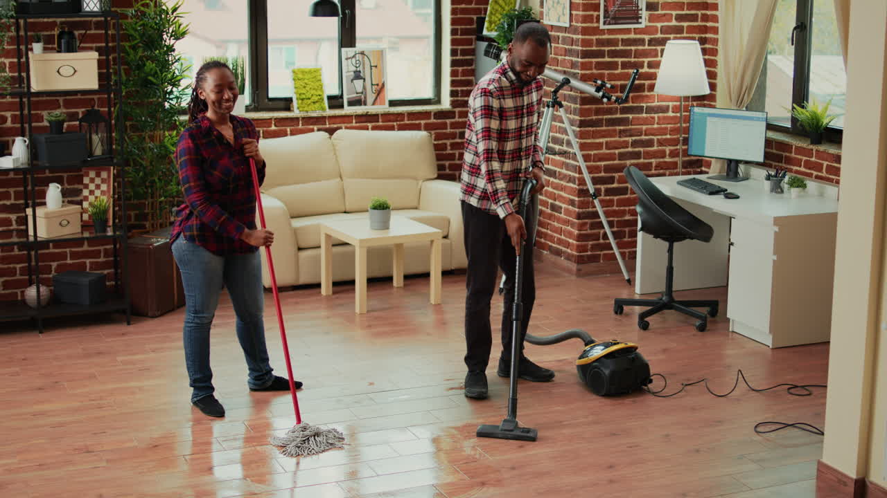 African american couple dancing and cleaning apartment rooms