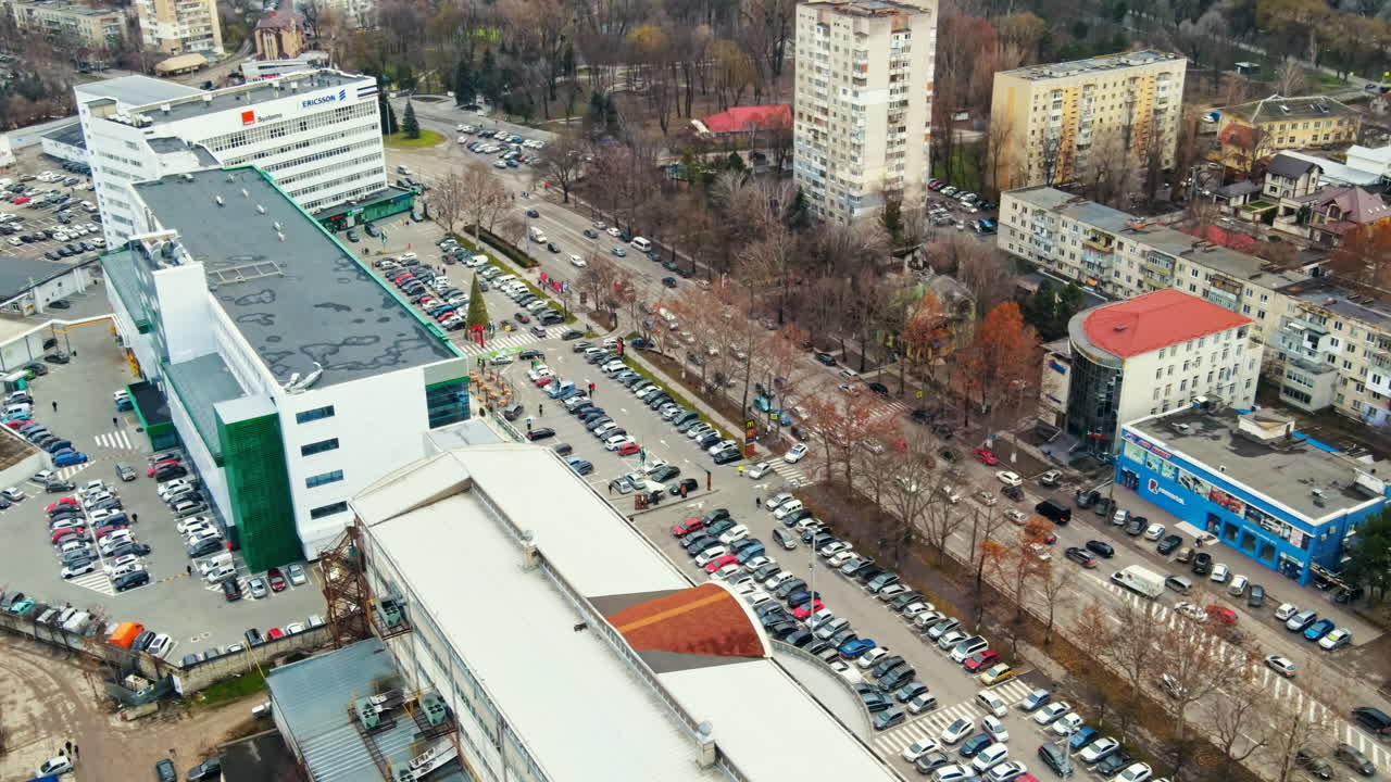 Aerial drone view of Chisinau. View of multiple buildings, road with moving cars, parking and bare trees along the street. Moldova