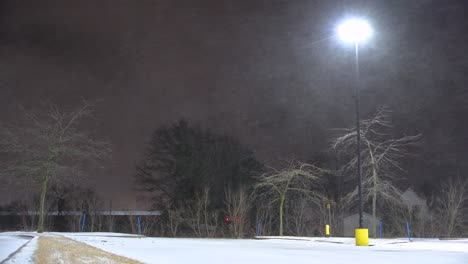 Blustering-snow-flurries-float-across-dark-sky-with-lone-street-lamp-in-Saint-Jean-sur-Richelieu,-Québec,-Canada