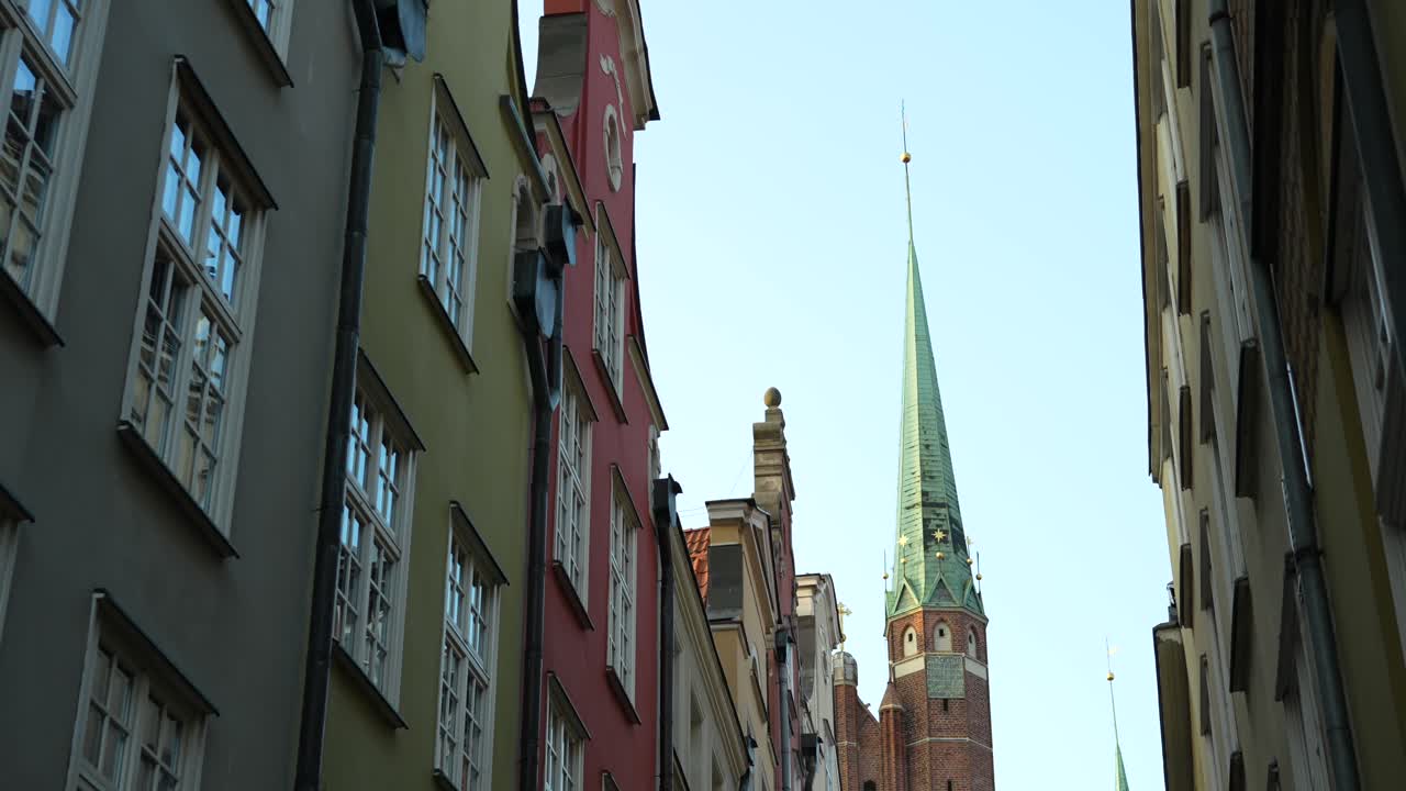View of tall Church spire from narrow street with colourful buildings in Gdansk