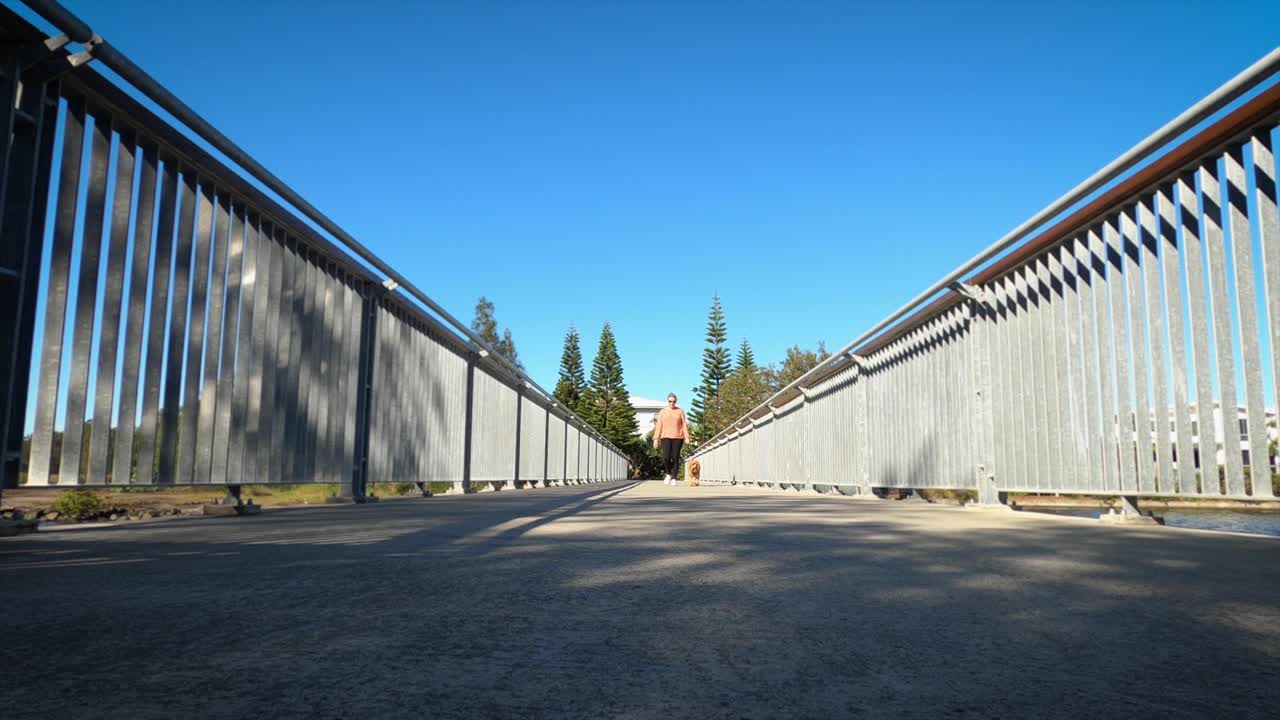 una mujer madura pasea a su perro por un puente peatonal en un suburbio costero de australia