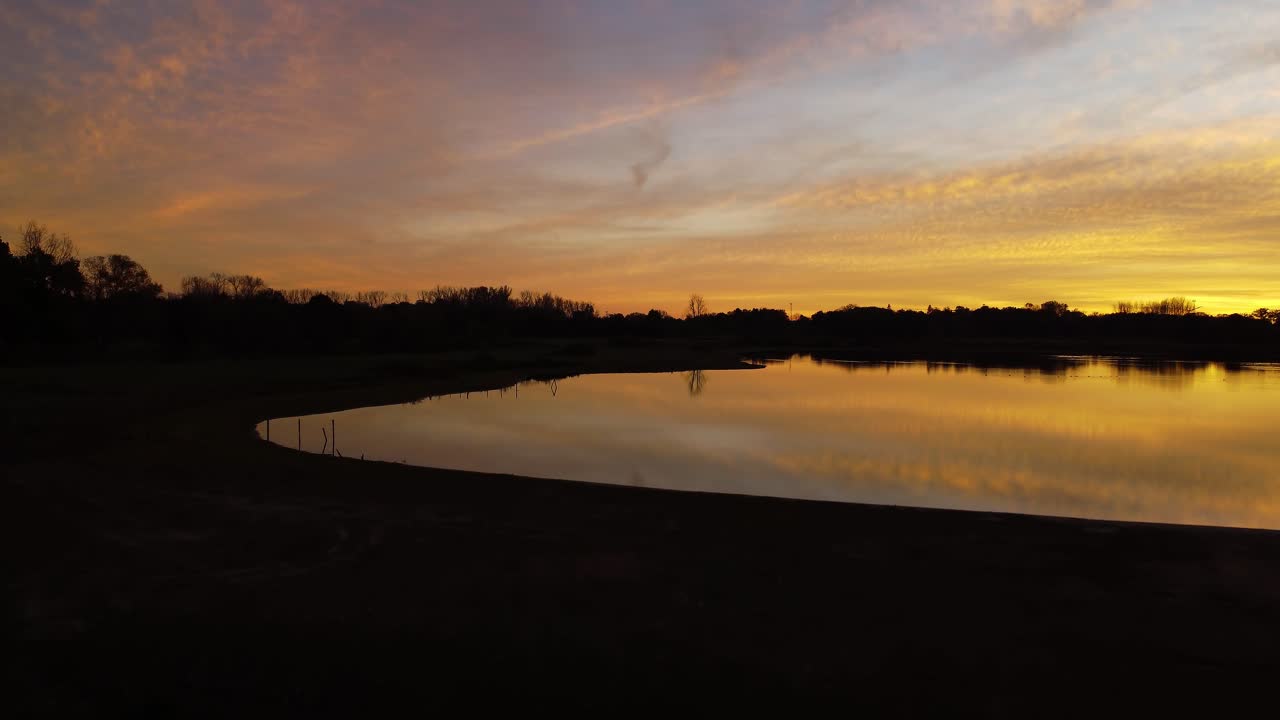 Rising from a dark shore the calm lake reflects the golden light of the sunset of Mechels Broek