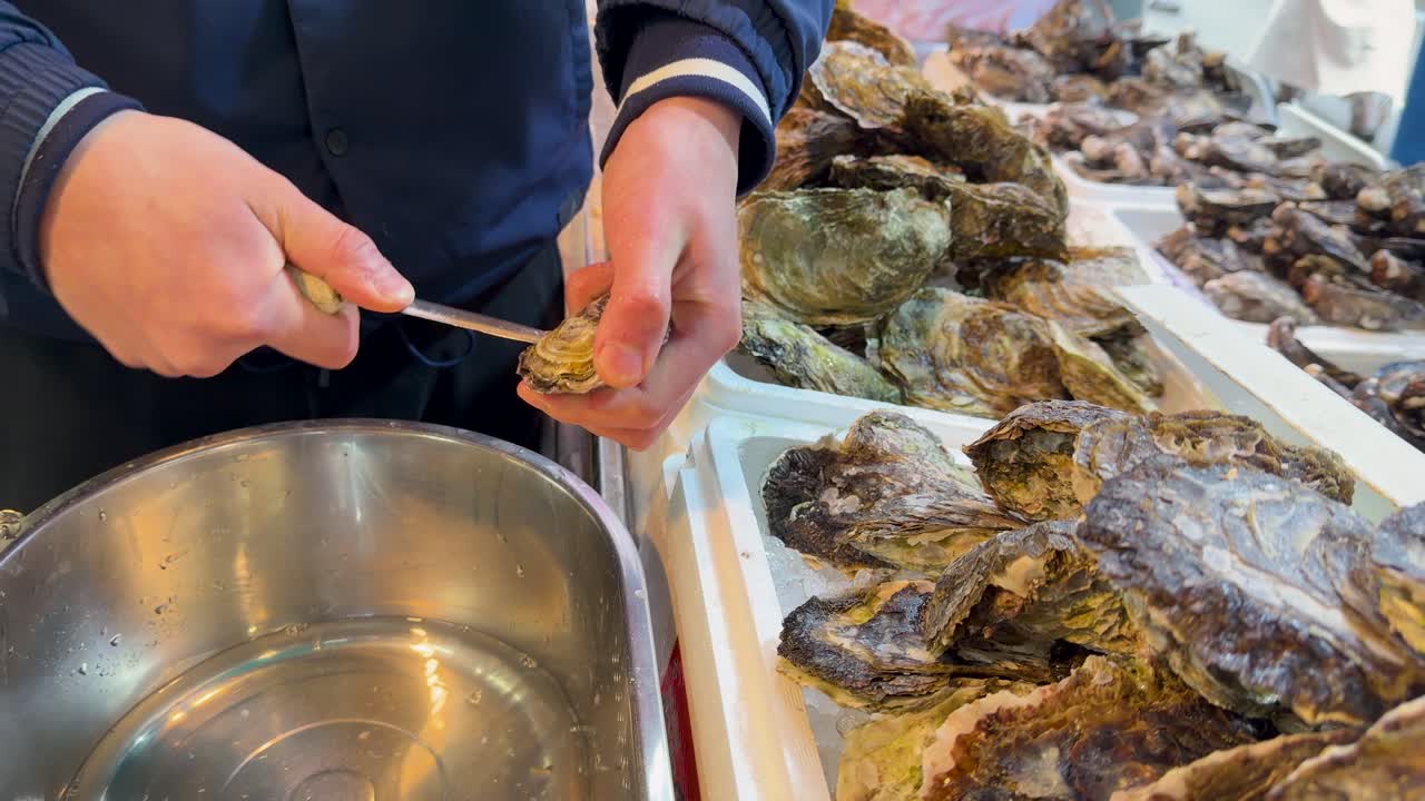 Close-up shot of a vendor using a knife to shuck fresh oysters in Tokyo