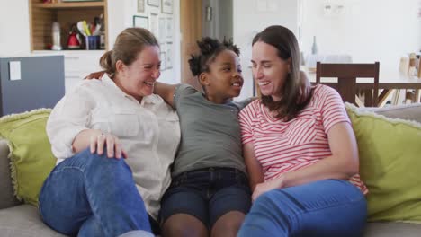 portrait of happy caucasian lesbian couple and their african american daughter embracing and smiling