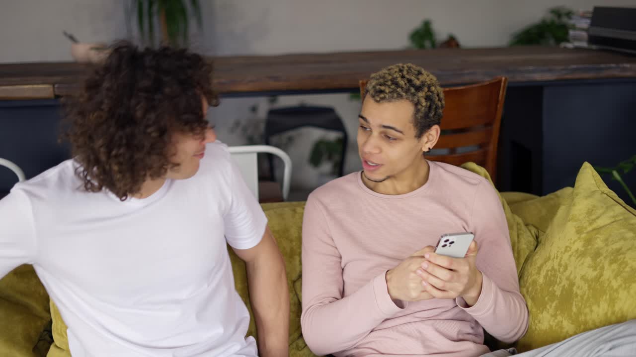 pareja gay relajándose en el sofá abrazándose, viendo la pantalla del teléfono inteligente