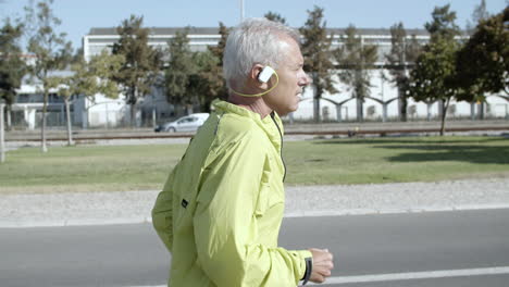 side view of active male pensioner with hearing aid device jogging outside