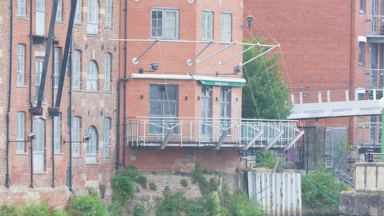 A smooth daylight camera pan reveals historic brick riverside buildings, metal balconies, and greenery in a calm urban environment with soft, diffused lighting