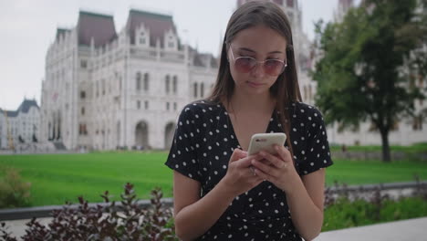 joven usando el teléfono frente al edificio del parlamento húngaro