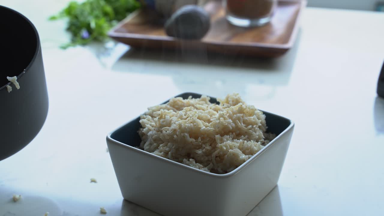 vapor que sale de un cuenco de arroz marrón para cocinar una comida dos latas de frijoles arroz plátano aguacate cebolla roja y cilantro