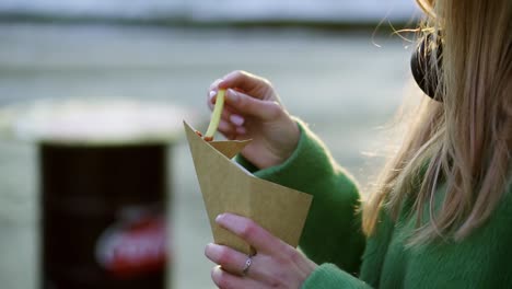 Woman-eating-french-fries-outdoors-on-winter-street-dip-in-ketchup