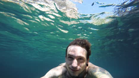 young man takes deep breath and dives underwater giving view from below in clear warm sea