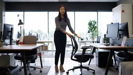 a professional setting: a focused individual adjusts their office chair amidst a modern workspace filled with desks, computers, and natural light