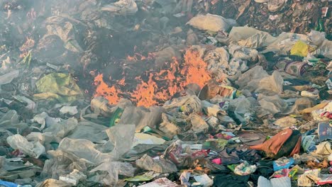 closeup shot of fire burning the garbage at the dump yard or land fill outside the city and polluting the air and environment