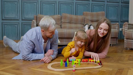 madre y padre jóvenes jugando con el niño hija montando el tren de juguete en el juego de ferrocarril de madera en casa