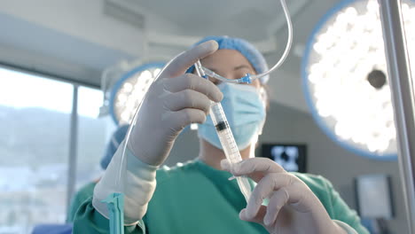 caucasian female surgeon filling drip with syringe in operating theatre, slow motion