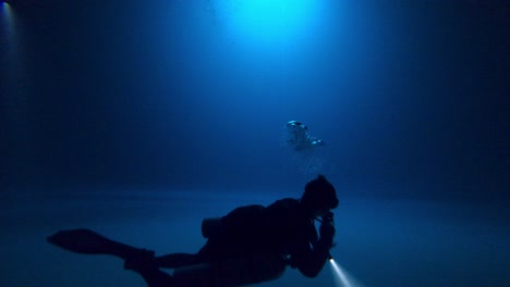 a technical cave diver calmly floating above a misty silt floor with a torch